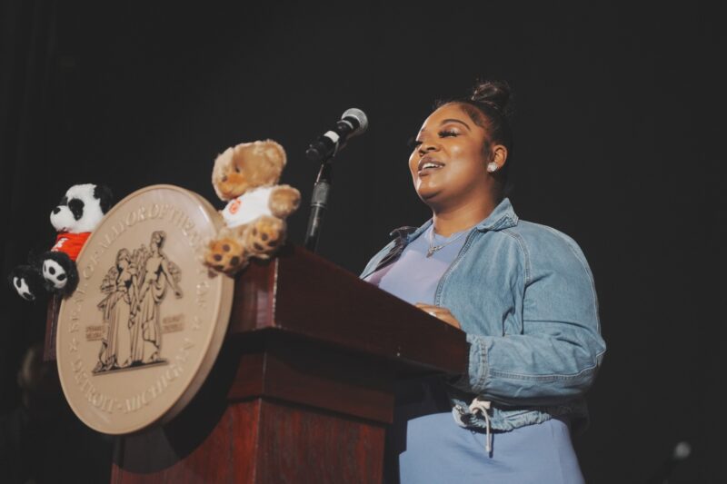 A mom speaking at a podium, smiling, wearing a blue dress and jacket