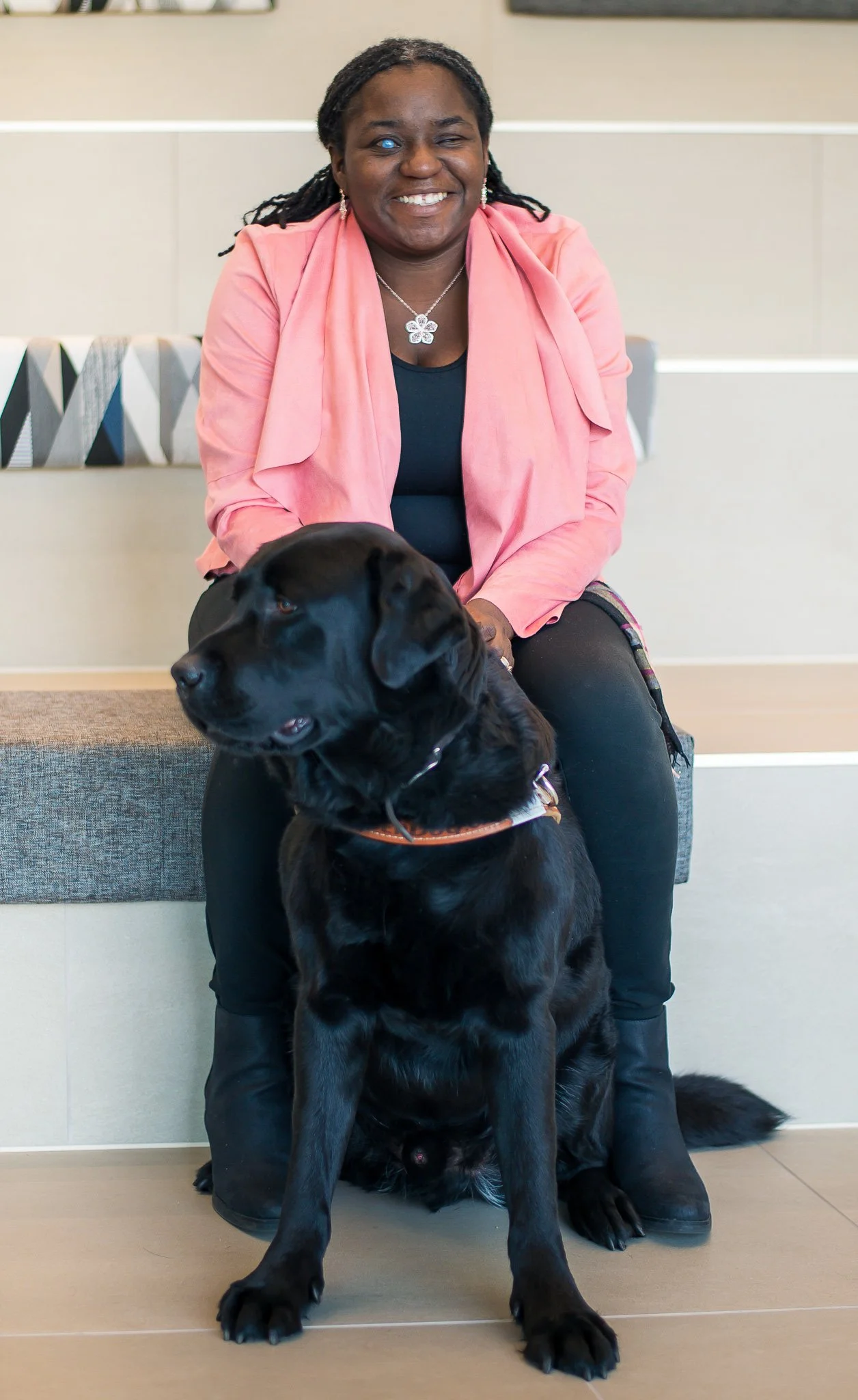 A woman in a pink jacket sitting behind a black dog