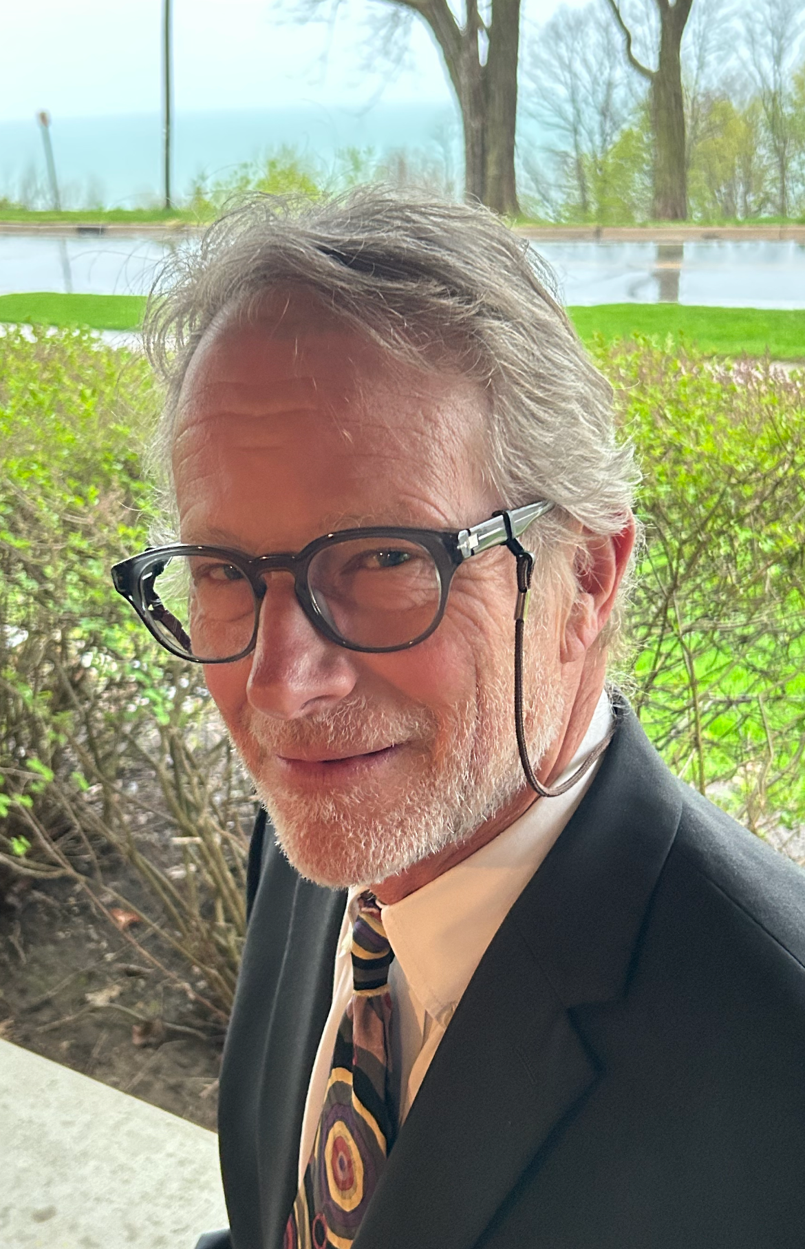 A man in a black blazer with glasses looking at the camera