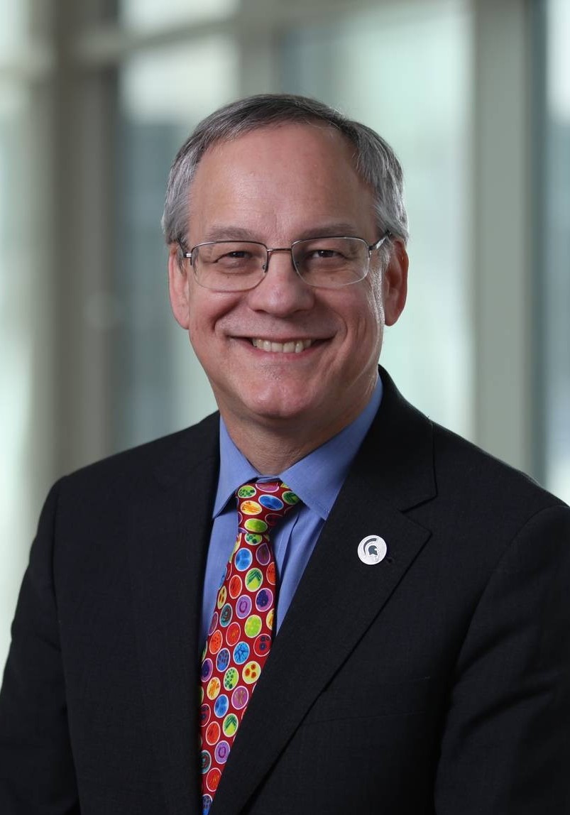 A smiling man in a blue shirt, black sport coat and red colorful tie