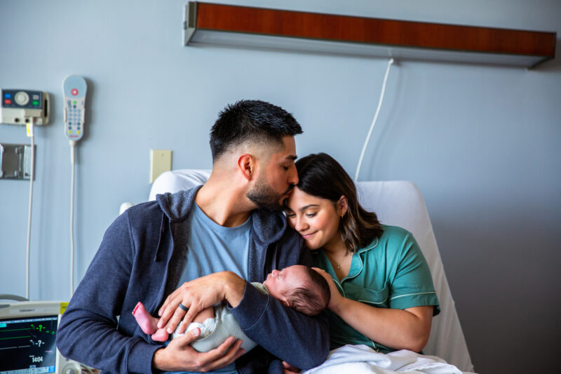 A photo of a man and woman holding a baby in a hospital