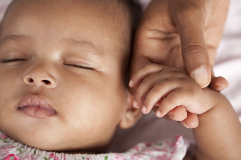 Close up portrait of 3 month old baby sleeping holding her mother hand.