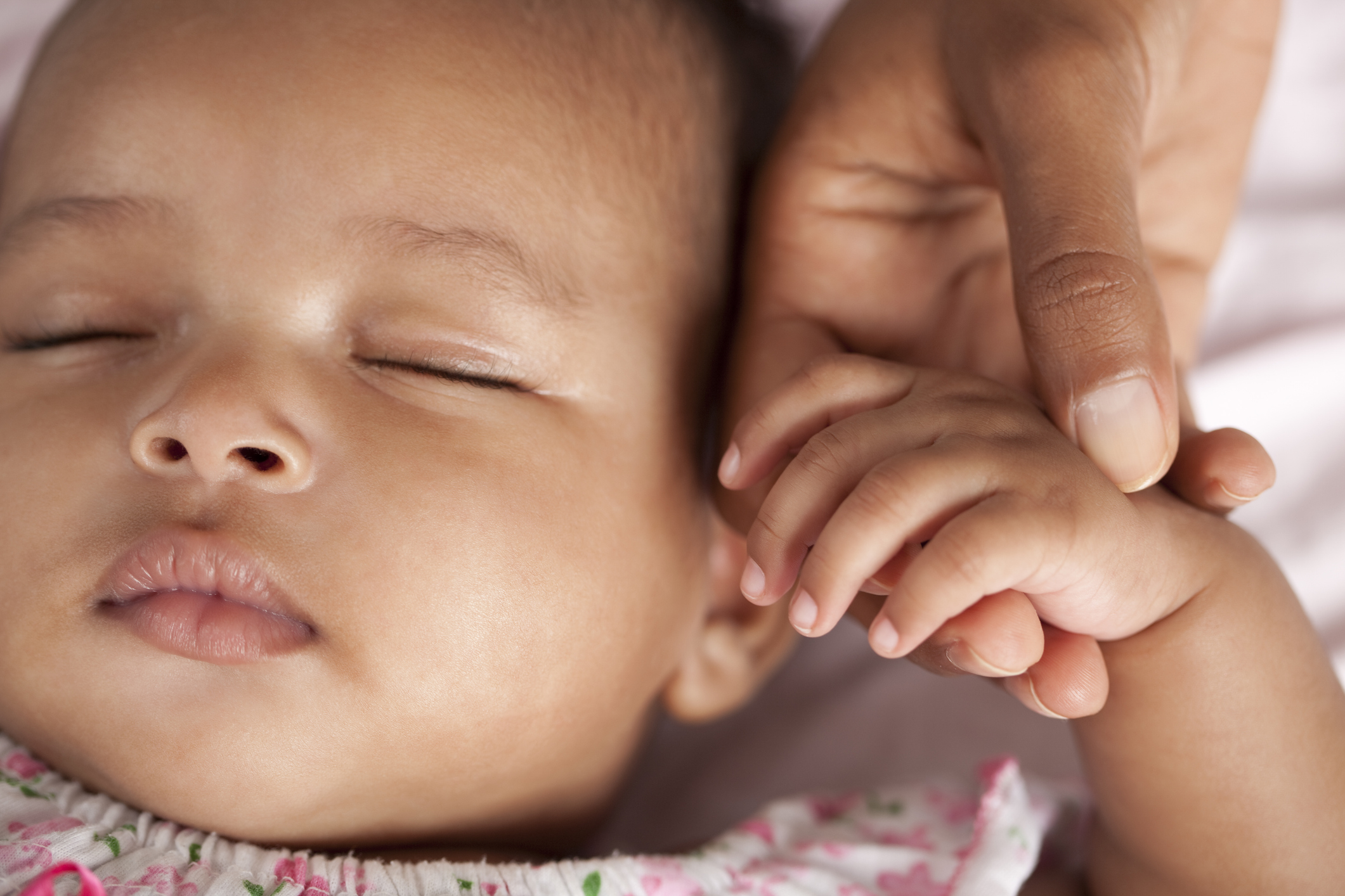 Close up portrait of 3 month old baby sleeping holding her mother hand.
