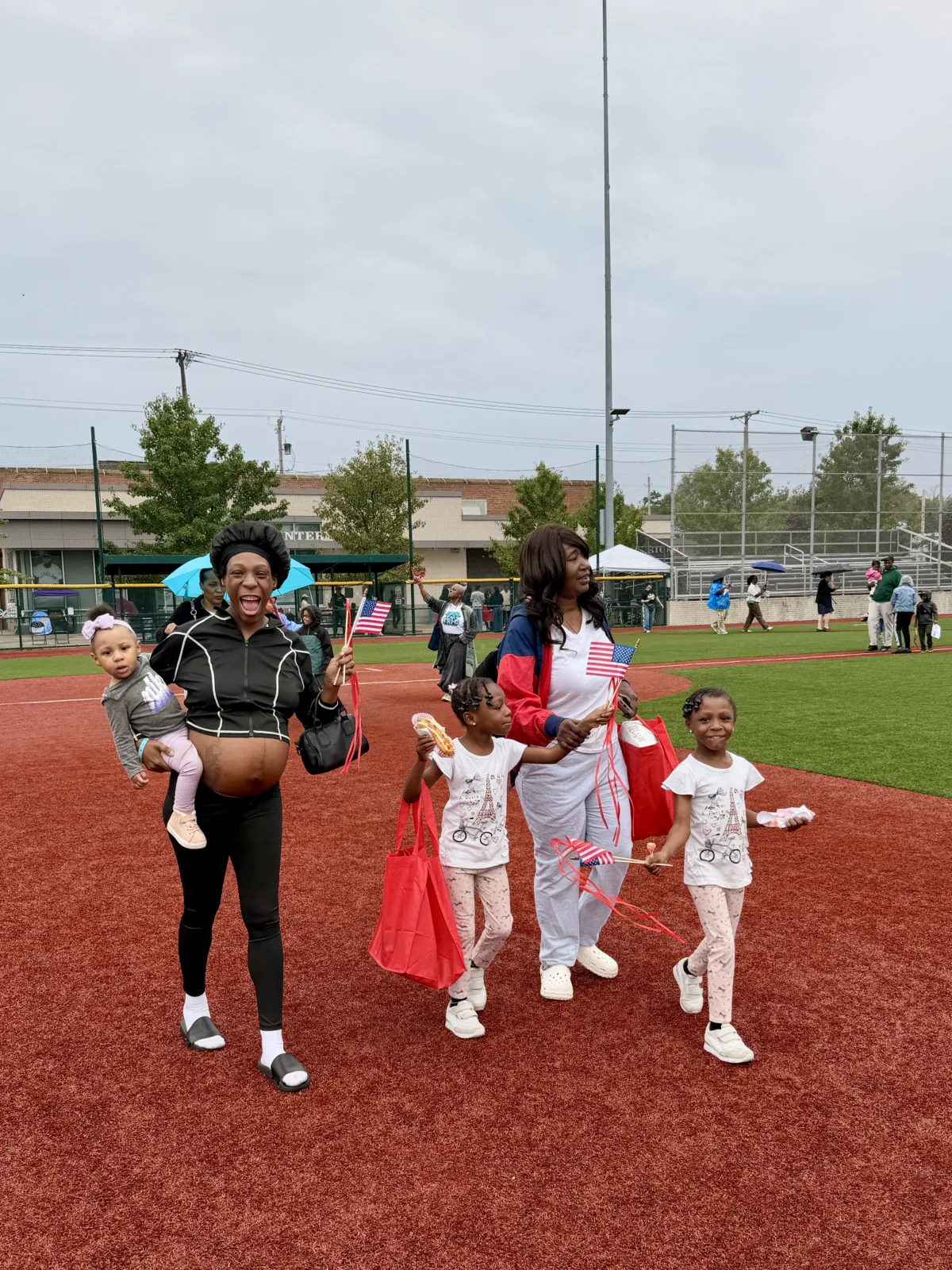 Two women and three children walking and smiling on a baseball field