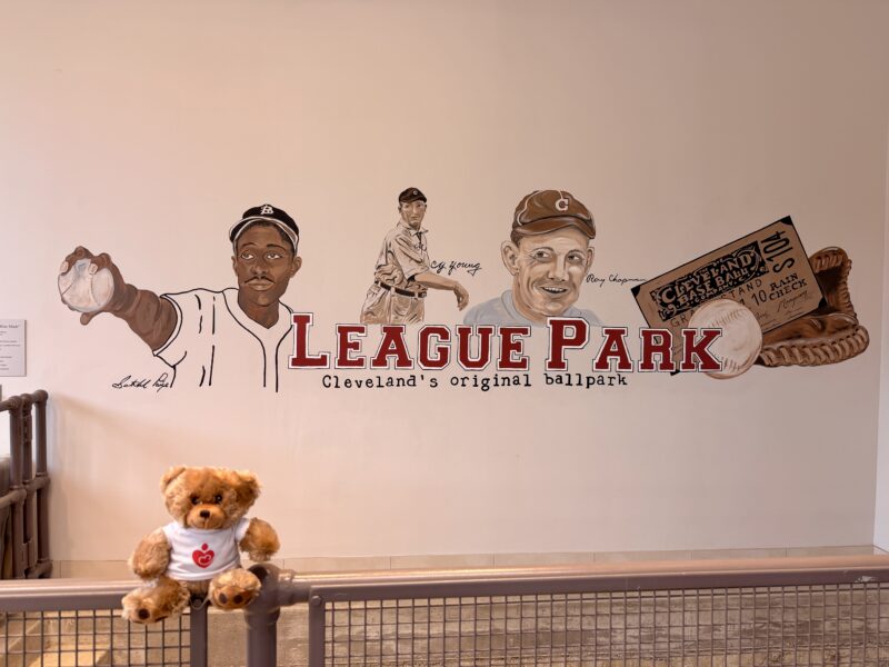 A teddy bear in front of a League Park sign